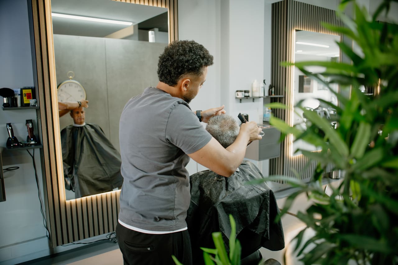 Barbeiro a trabalhar o cabelo de um cliente, visto de lado por entre as plantas