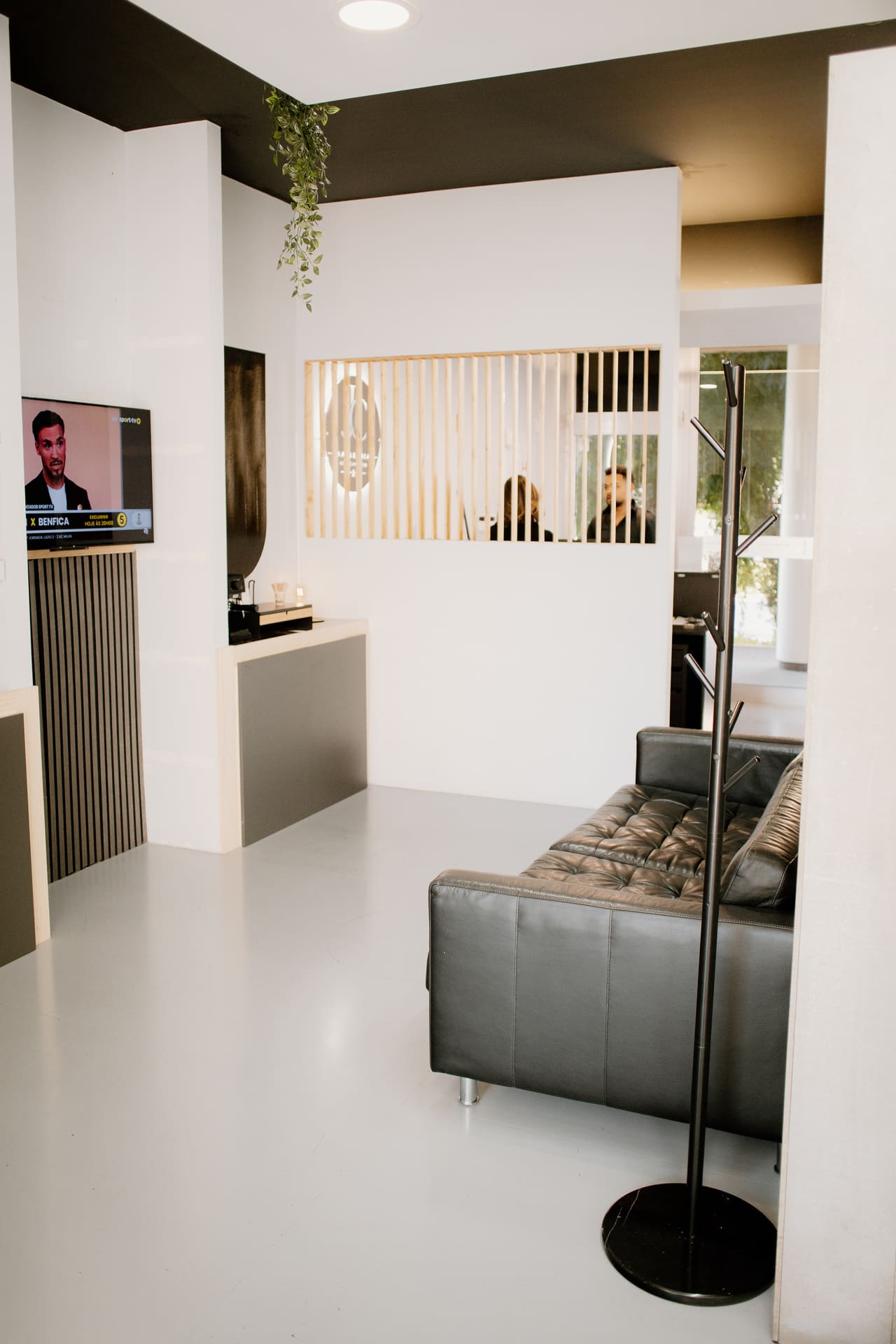 Sala de espera com sofá de pele, televisão e divisória ripada